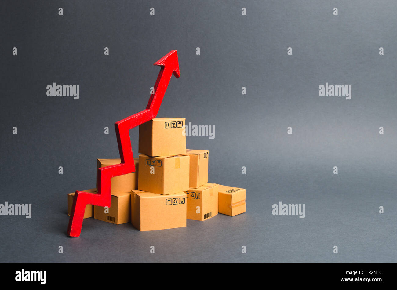 A pile of cardboard boxes and a green up arrow. The growth rate of production of goods and products, increasing economic indicators. Increasing consum Stock Photo