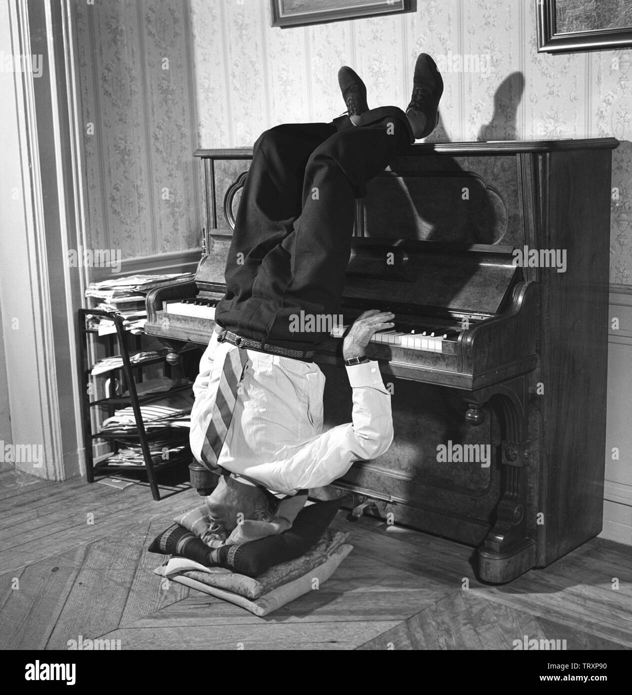 Man in the 1950s. With nothing else to do, this man finds that playing the piano standing upside down, works for him. Sweden 1950s ref BV91-8 Stock Photo