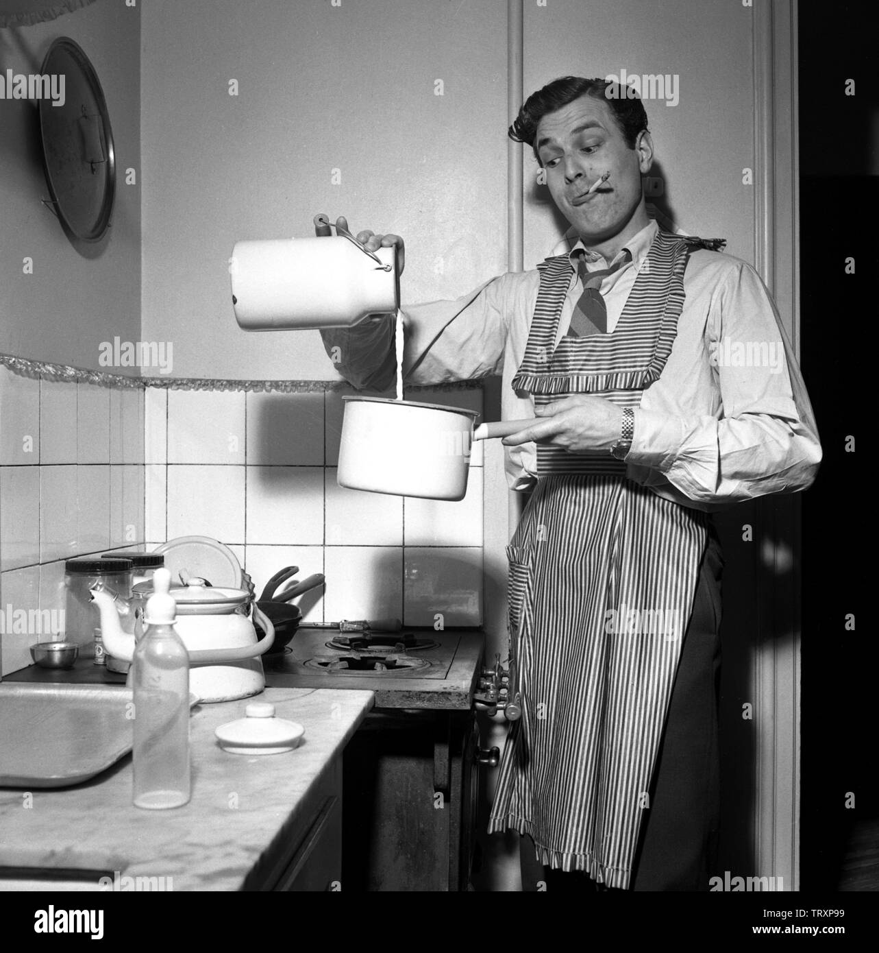 Man of the 1950s. The swedish dancer Mario Mengarelli in the kitchen busy pouring milk into a saucepan. A feeding bottle is seen on the bench and could be that his small child is waiting for a meal. Sweden 1952 ref 1958 Stock Photo