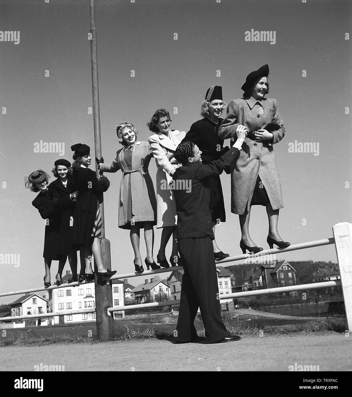 Women of the 1940s. Seven young women are balancing on a fence. A man is giving a hand. Picture taken in the town Borås where the saying is that there is a shortage of single men.  Only one free and single man on seven women.  Sweden 1942. Photo Kristoffersson ref A42-5 Stock Photo