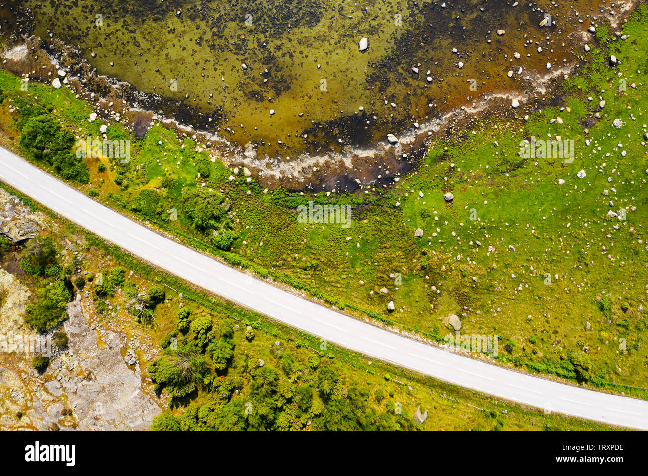 Top down aerial of island grass shoreline littered with boulders. A country road cuts through the landscape. Location Blekinge in Sweden. Stock Photo