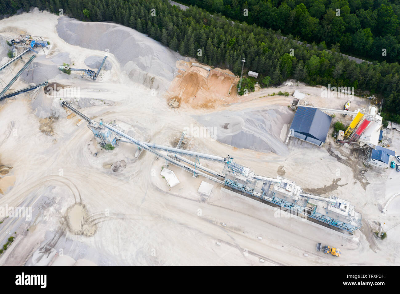 Aerial of cement and concrete industry in a quarry beside a forest and a road. Stock Photo