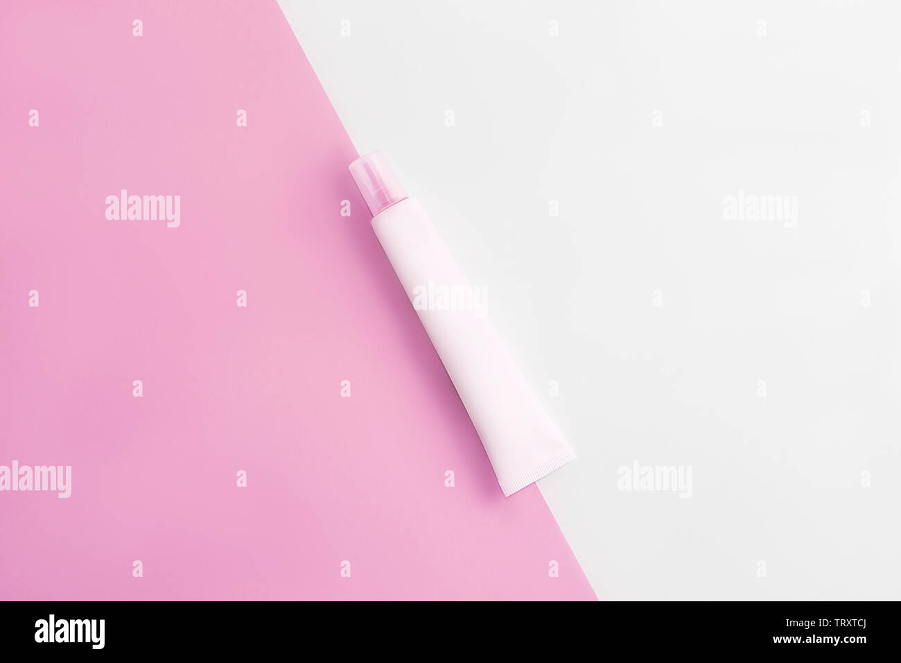 Cosmetics tube on pastel pink and white background. Copy space. Flat lay. Beauty industry concept. Stock Photo
