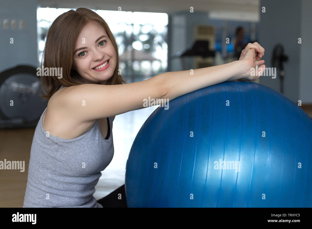 Smiling young caucasian woman girl on blue gymnastic ball at the gym, doing workout or yoga pilates exercise Stock Photo