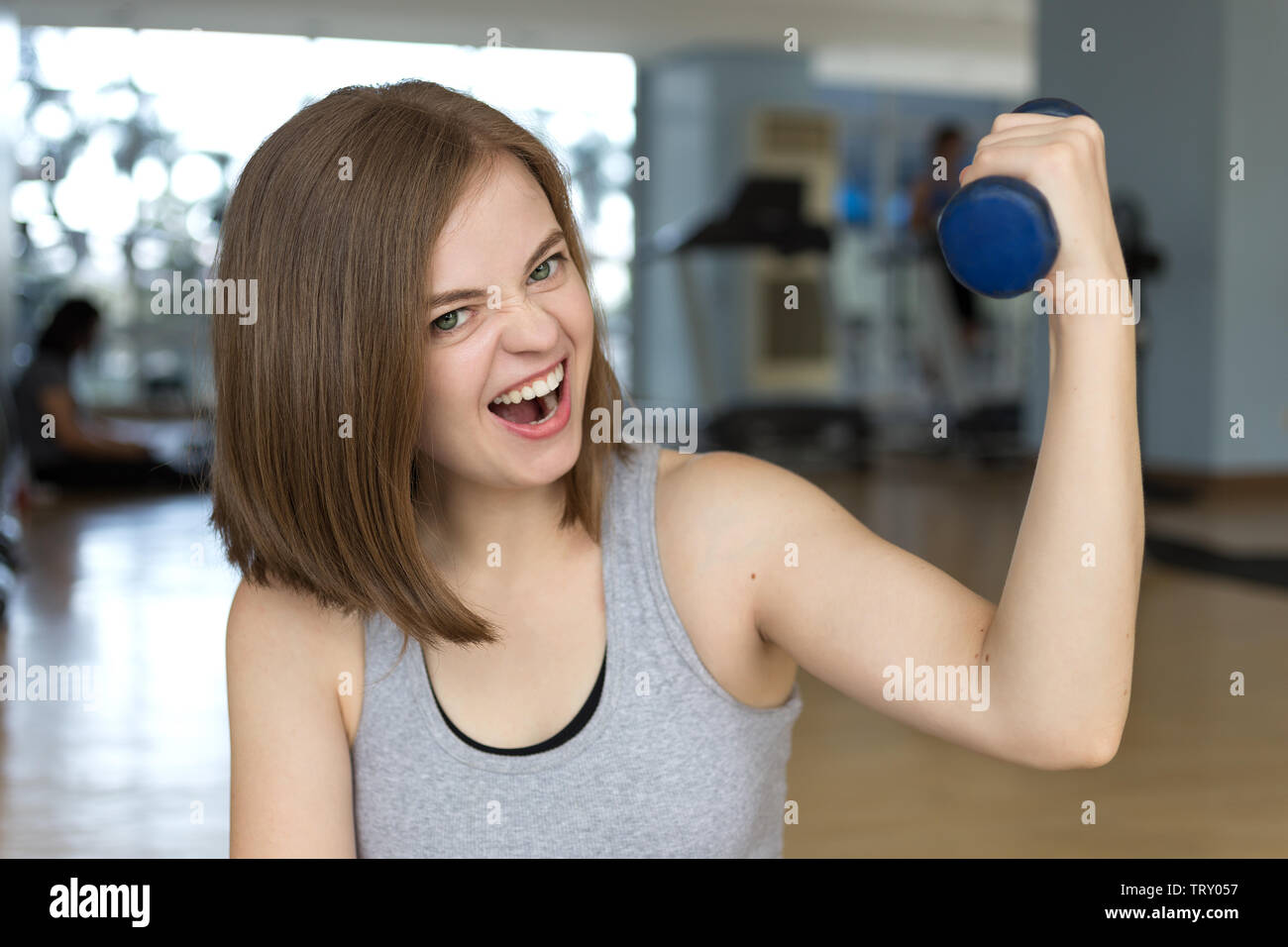 Smiling young caucasian woman girl doing workout with light dumbbells at the gym, lifting weights Stock Photo