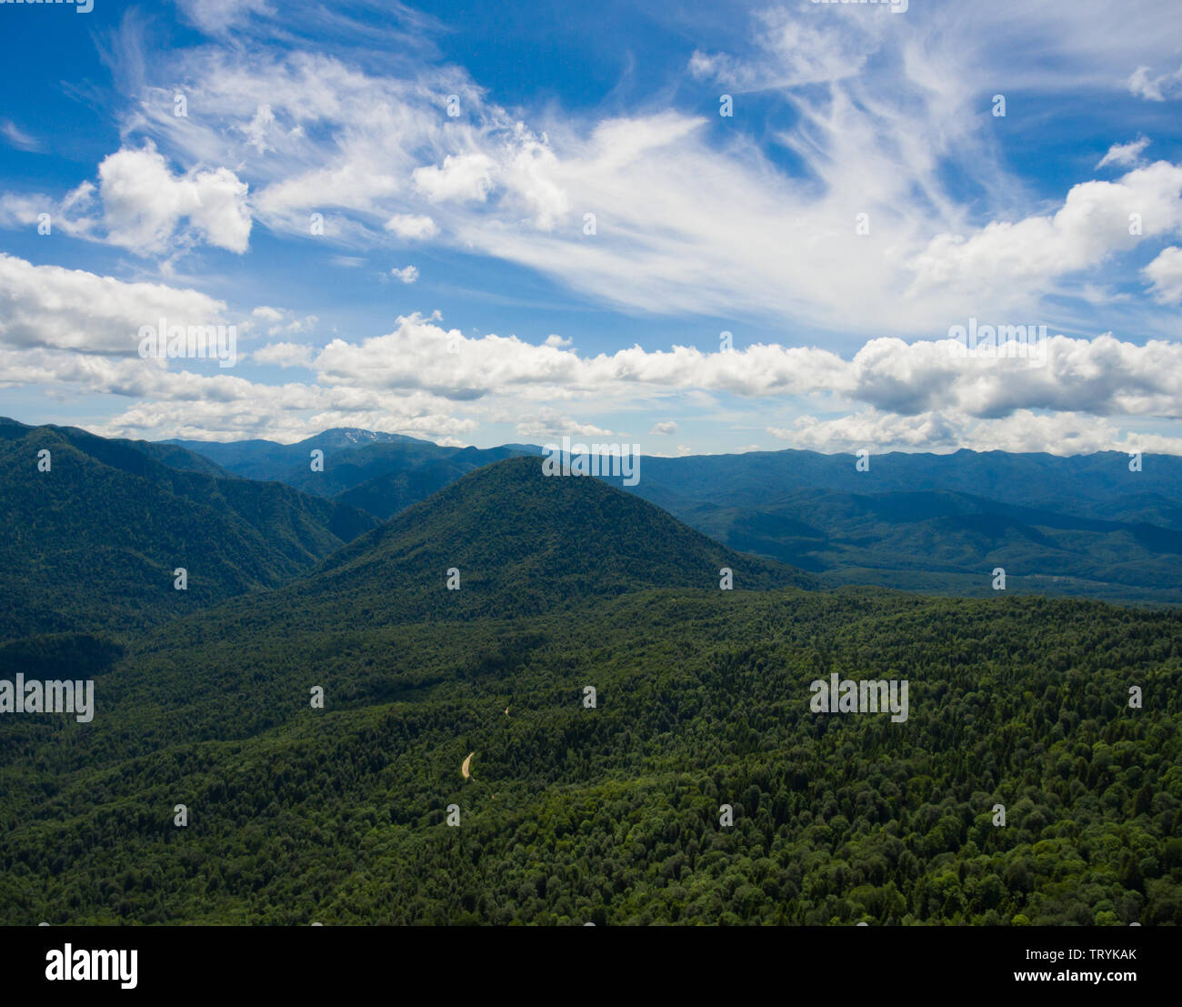 Aerial photo. Beautiful mountain valley. Summer landscape with mountain peaks covered with forest; cloudy sky and a segment of the road through the fo Stock Photo