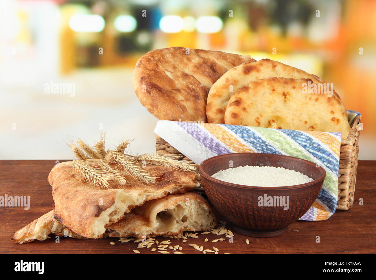 Pita breads in basket with spikes and flour on table on bright