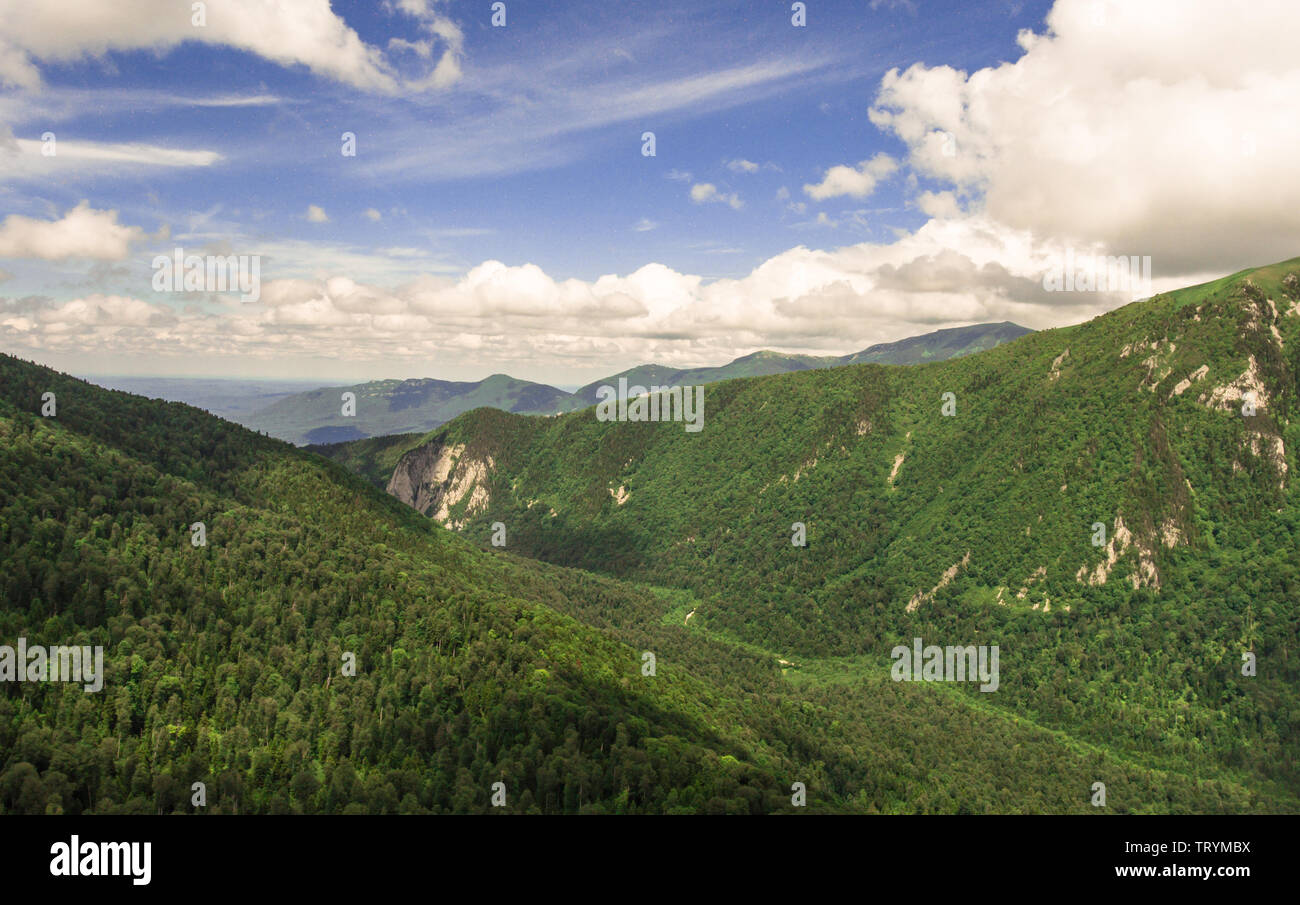Aerial photo. Beautiful mountain valley. Summer landscape with mountain peaks covered with forest and a cloudy sky. Caucasus mountain system. Stock Photo