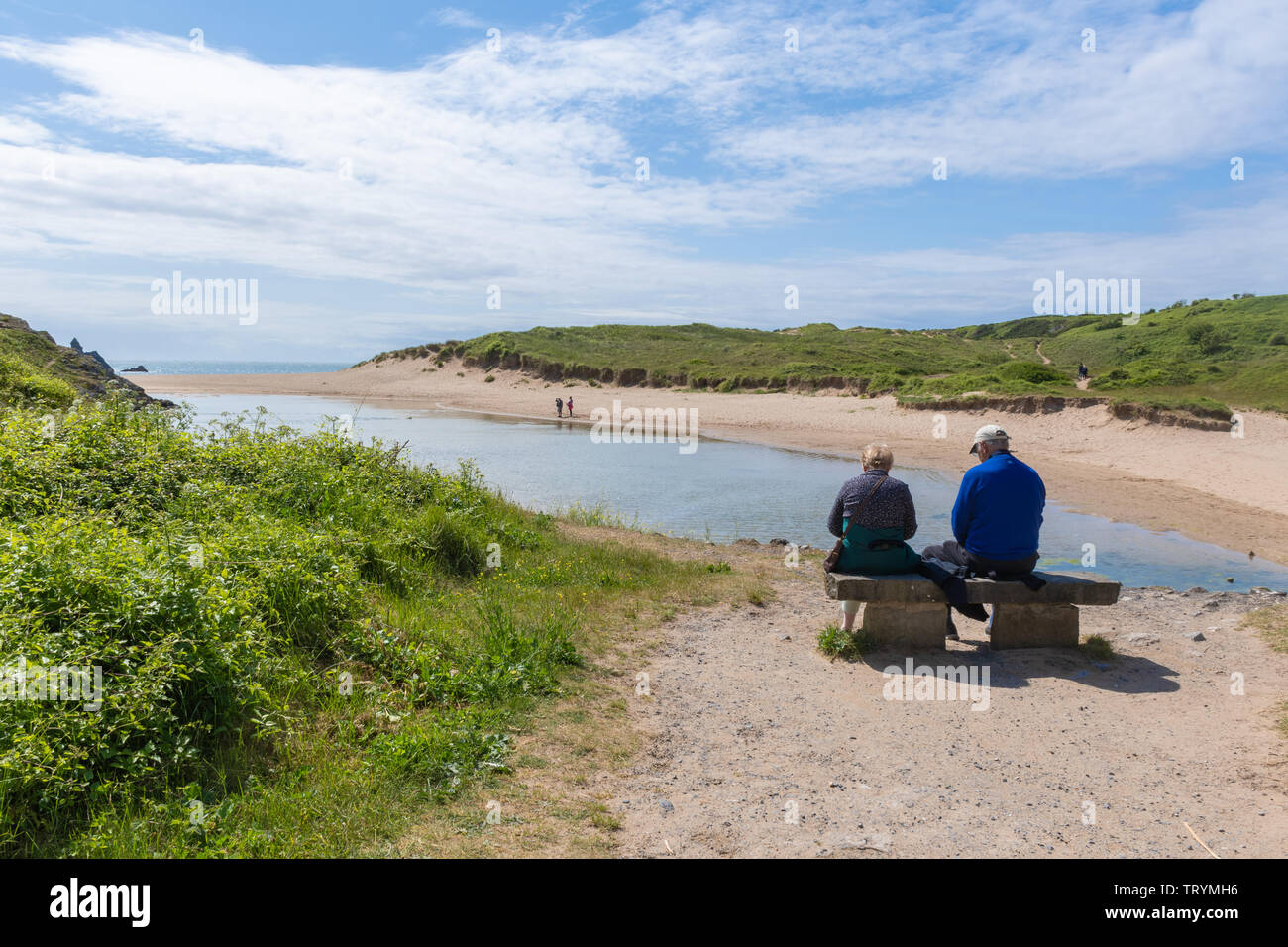 Older couple sitting on a bench enjoying the view of Broad Haven beach on the Pembrokeshire coast, Wales Stock Photo
