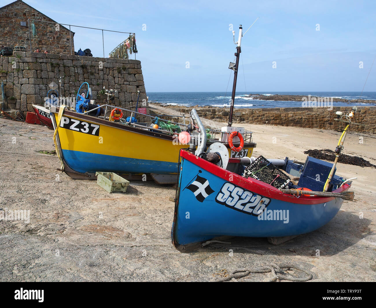A group of very colourful fishing boats hauled up on to the quay at Sennen Cove, Cornwall, England, with the blue sky and blue sea beyond. Stock Photo