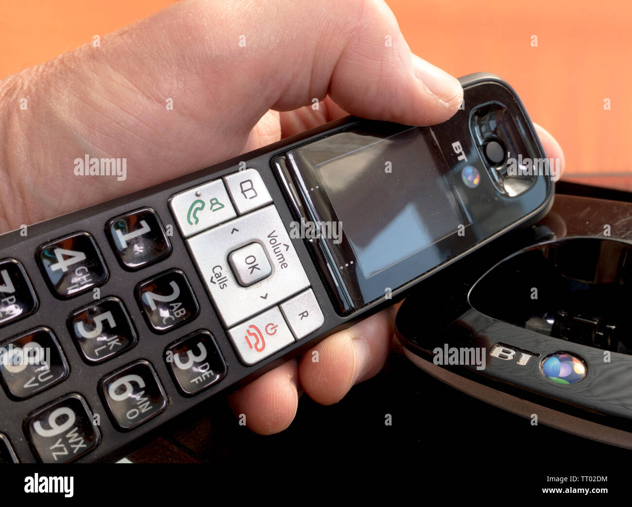 Man’s hand holding a BT hands free landline telephone next to its cradle, about to make a phone call. Stock Photo
