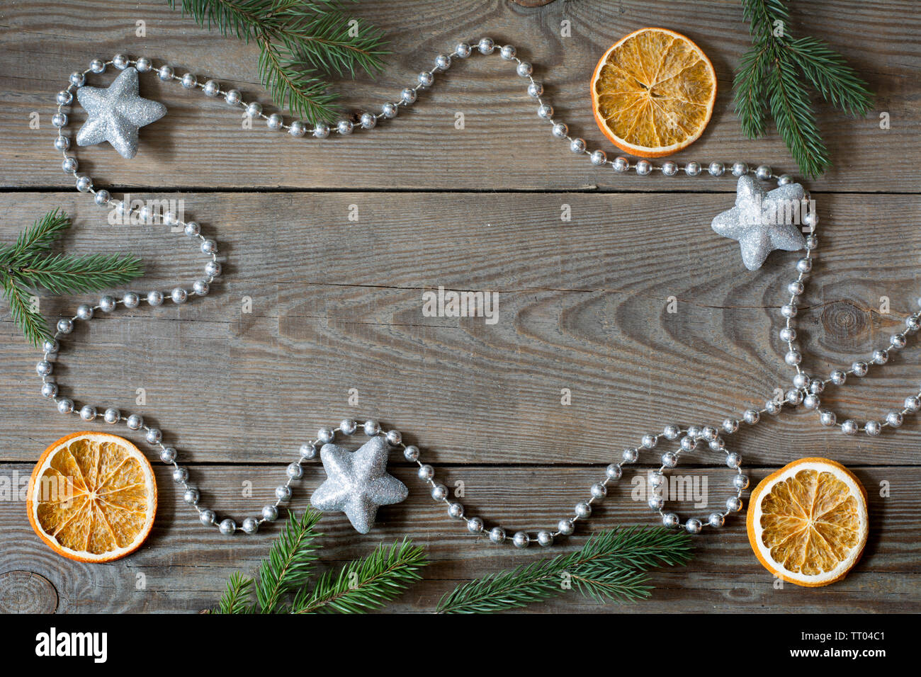 Christmas composition with silver bead chain, brocade stars, orange slices and fir tree branches on wooden background Stock Photo