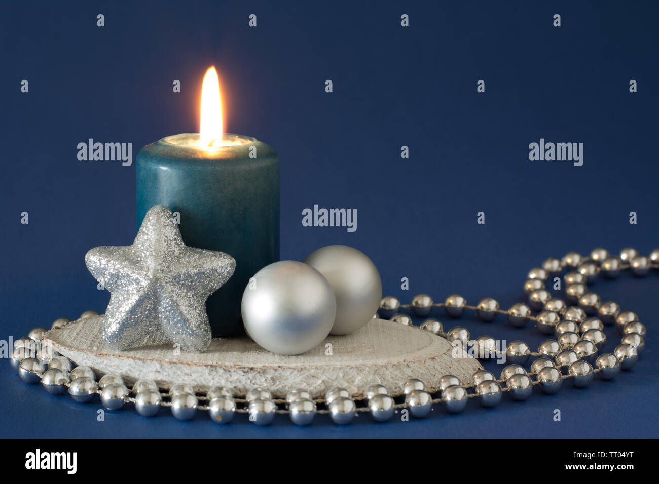 Silver and blue christmas composition with burning candle, glitter star, two baubles and bead chain on dark blue background - text space Stock Photo