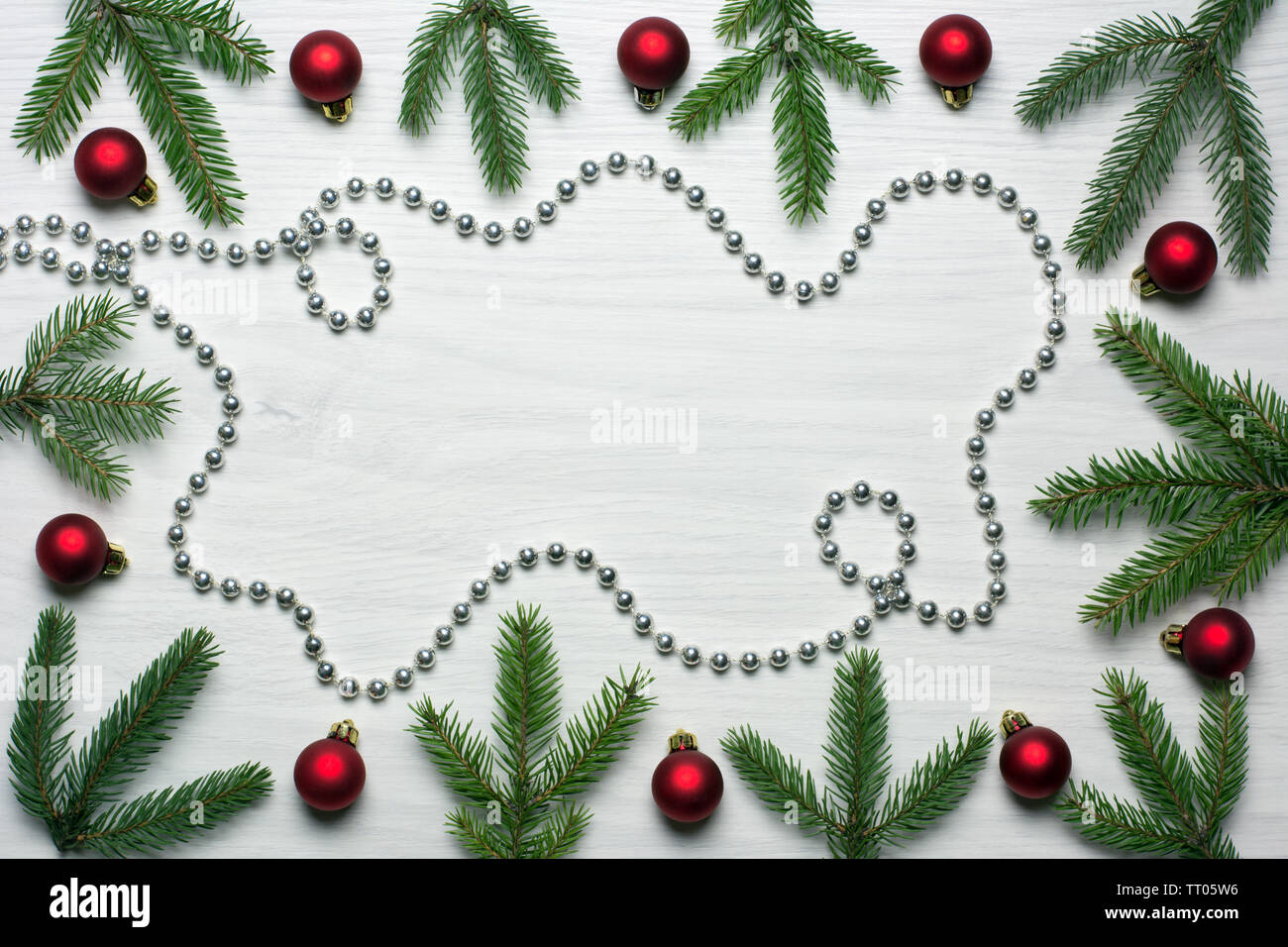 Christmas card concept with fir tree branches, red baubles and silver bead chain on white wooden background - text space Stock Photo