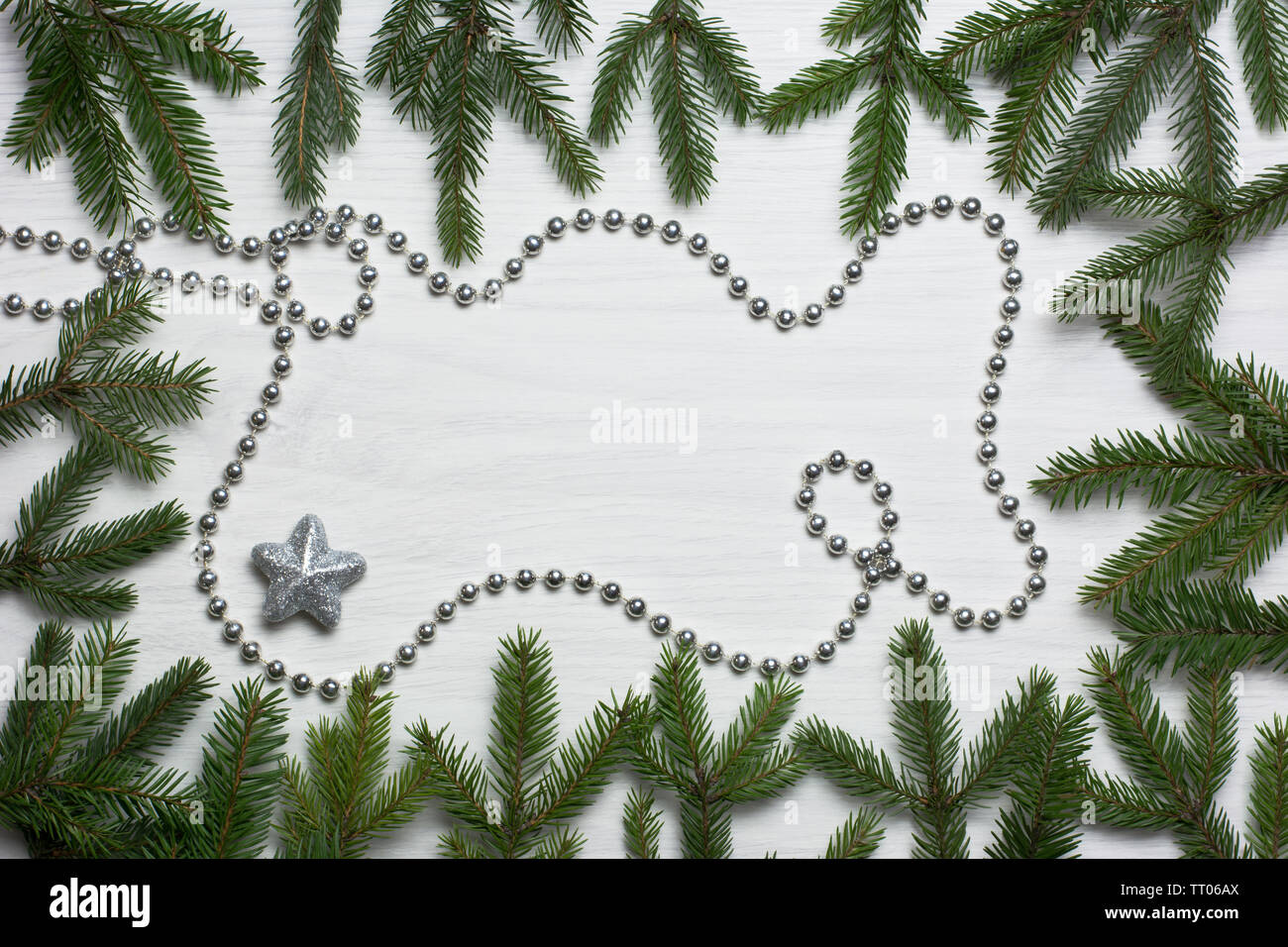 Christmas card concept with fir tree branches, one brocade star, and silver bead chain on white wooden background - text space Stock Photo