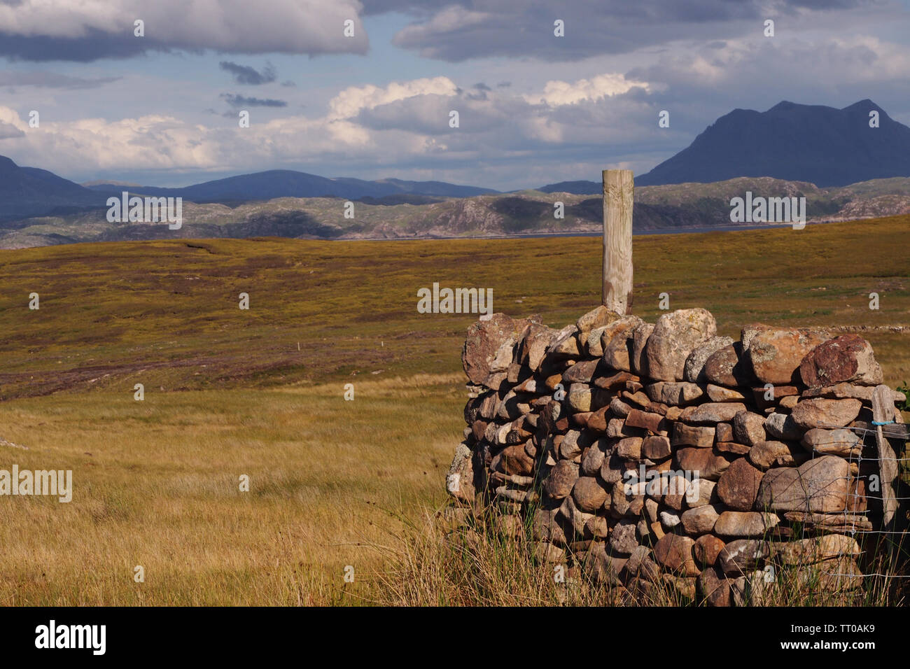 A landscape view of mountains and sky in the distance and a dry stone wall in the foreground and heathland on the Coigach Peninsula, Scotland Stock Photo