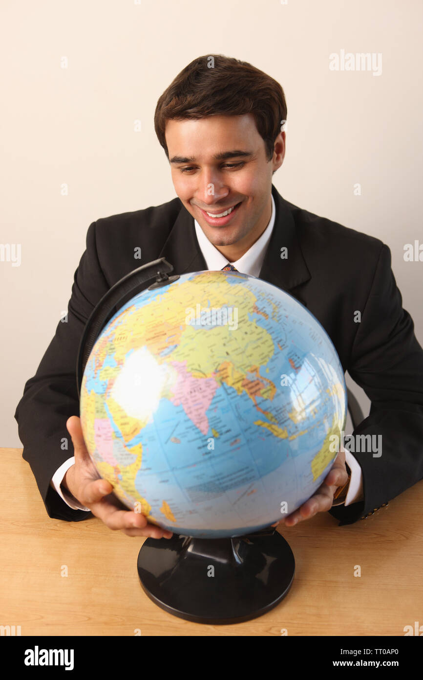 Businessman Looking At A Desktop Globe And Smiling Stock Photo - Alamy