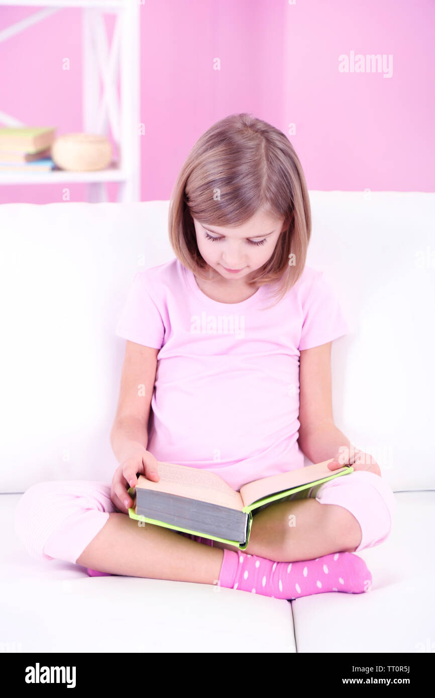 Little girl reading book sitting on sofa in room Stock Photo - Alamy