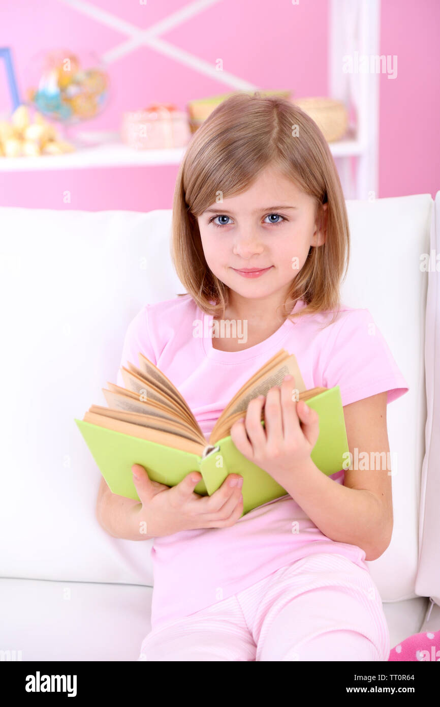 Little girl reading book sitting on sofa in room Stock Photo - Alamy
