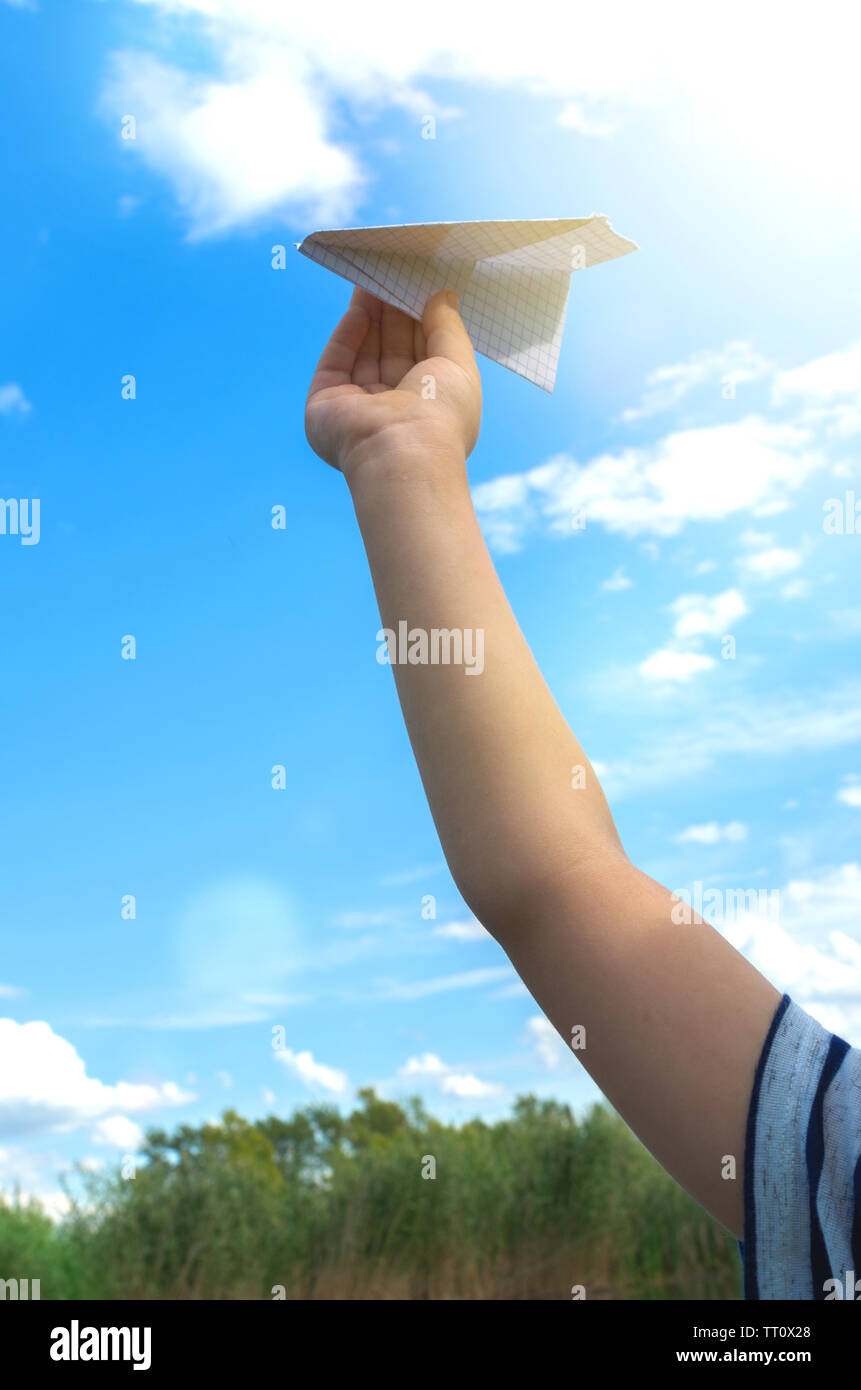 Hand of little boy runs paper airplane in the sky.On bright Sunny day ...
