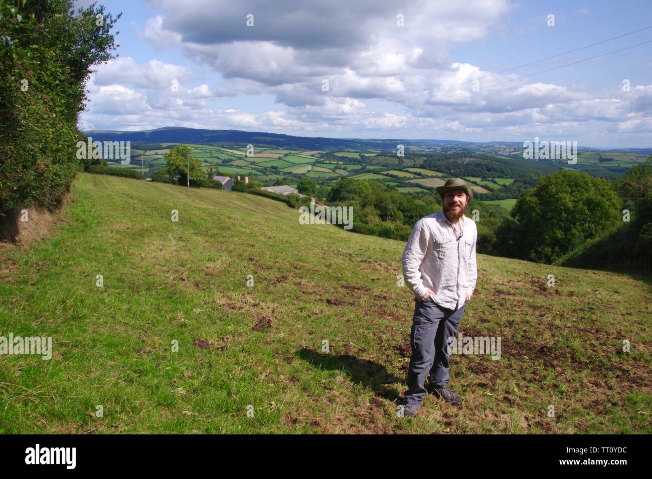 Bearded Outdoors Man in a Pastoral Patchwork Landscape of Fields, Hedgerows and Woods in High Summer. Buckfastleigh, Devon, UK. Stock Photo