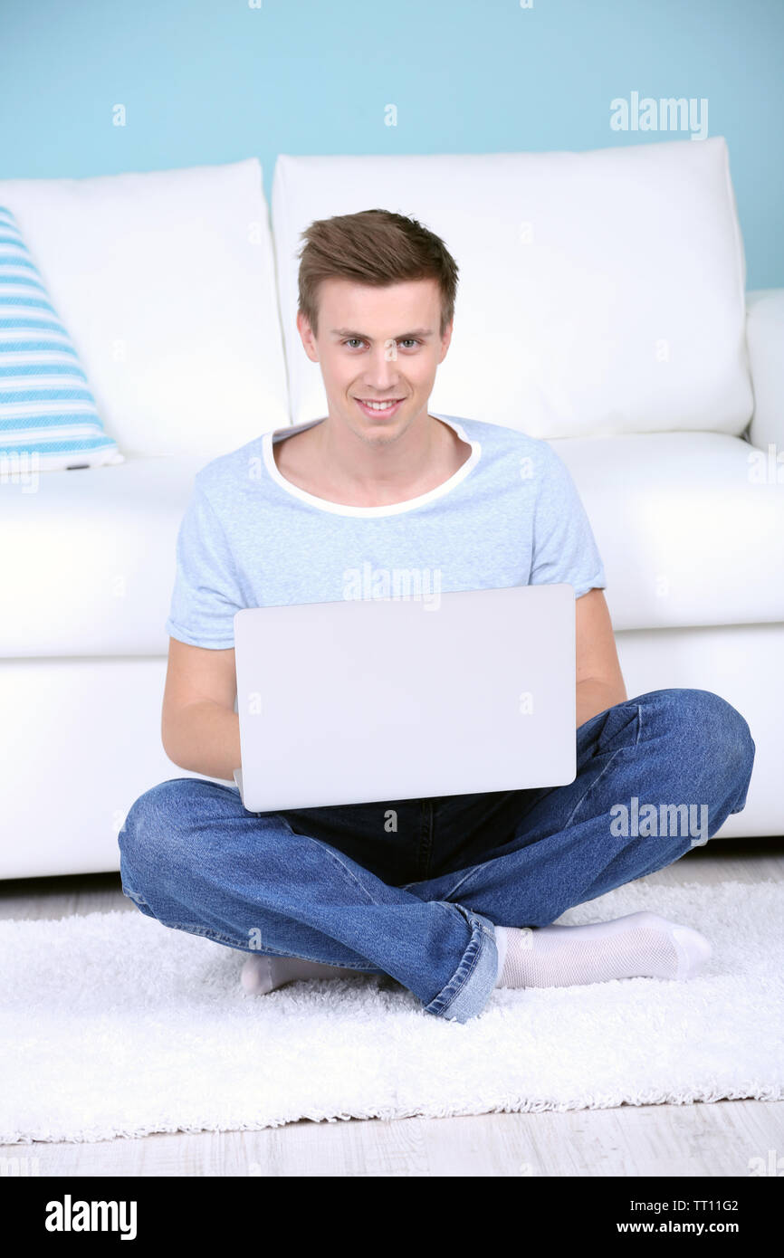 Guy sitting on floor with laptop on room background Stock Photo - Alamy