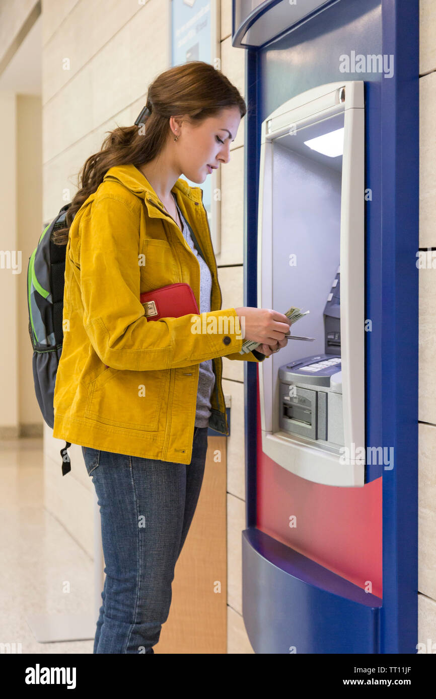 Young woman college university student getting cash money at bank ATM. Personal finance electronic banking concept. Stock Photo
