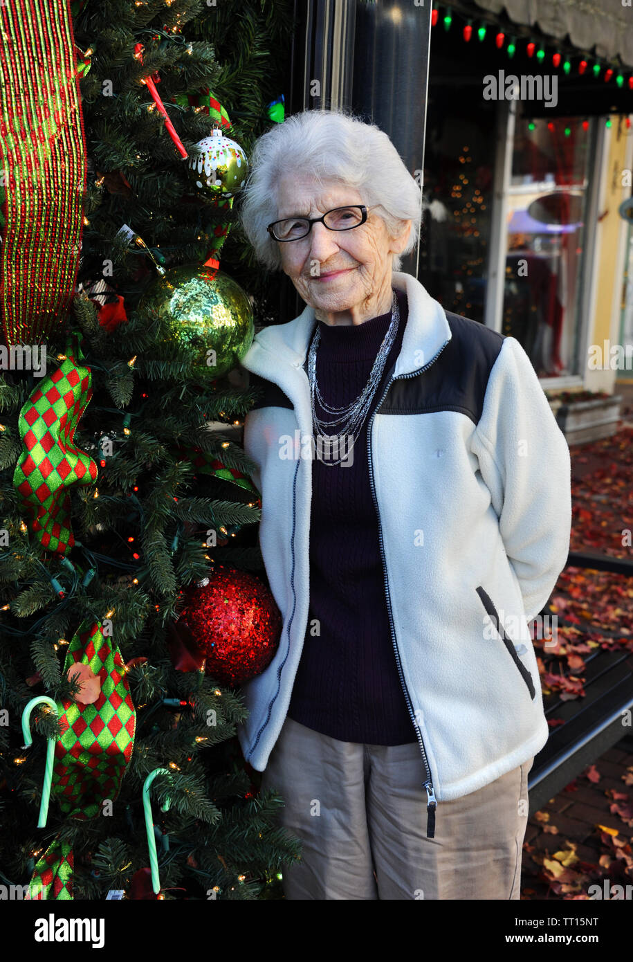 Grandmother, with white hair and glasses, stands besides a Christmas street decoration while shopping in downtown El Dorado, Arkansas.  She has on tan Stock Photo