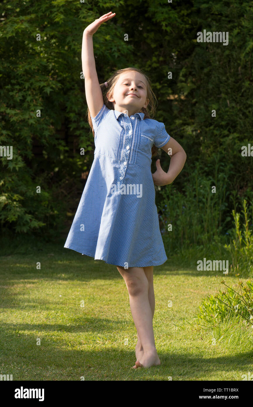 eight year old girl dancing in school uniform dress after school in garden posing for the camera, full of confidence Stock Photo