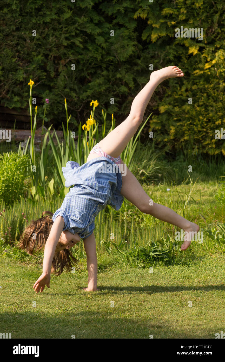 eight year old girl doing cartwheels in school uniform dress after school in garden practicing gymnastics Stock Photo