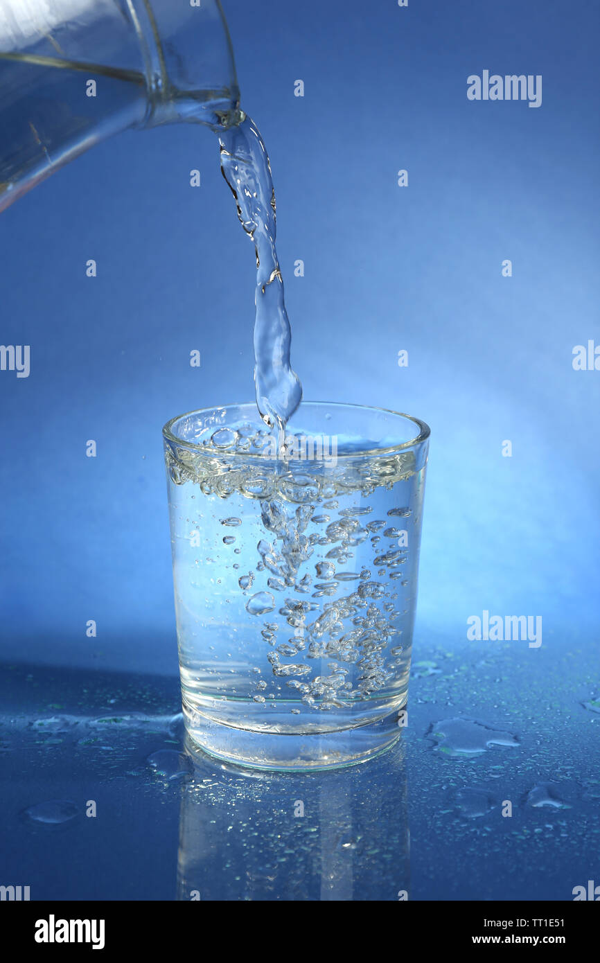 Pour water from pitcher into glass, on dark blue background Stock Photo