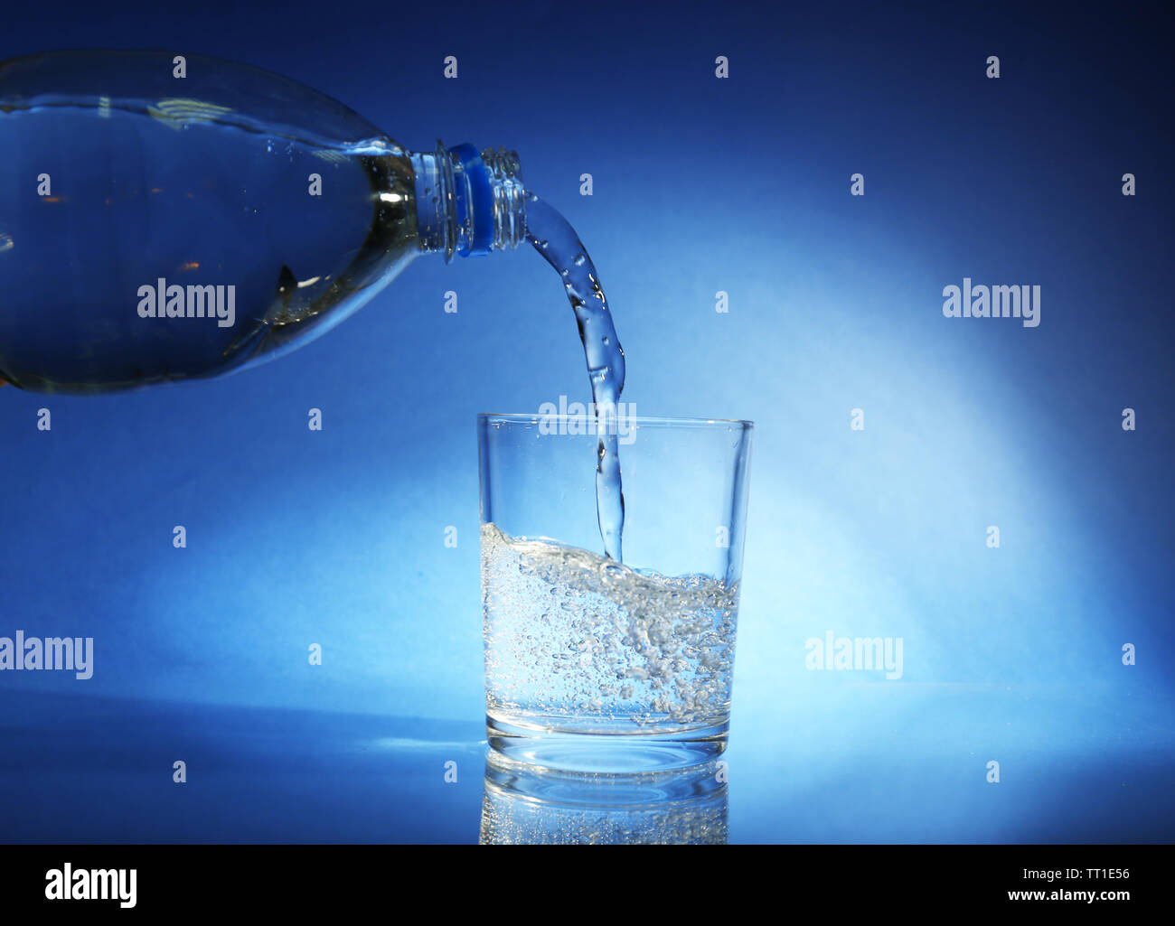 Pour water from bottle into glass, on dark blue background Stock Photo