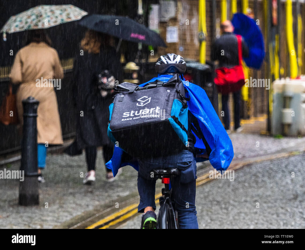 A Stuart company food delivery courier rides through London rain. Stuart is competing with Deliveroo and Uber Eats in this competitive market Stock Photo