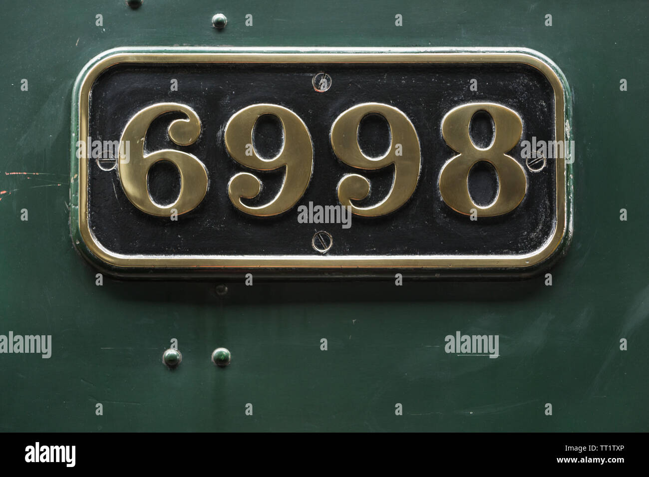 Embossed polished brass number plate sign fixed to green steam engine locomotive number 6998 'Burton Agnes Hall' at Didcot Railway Centre, Oxfordshire Stock Photo