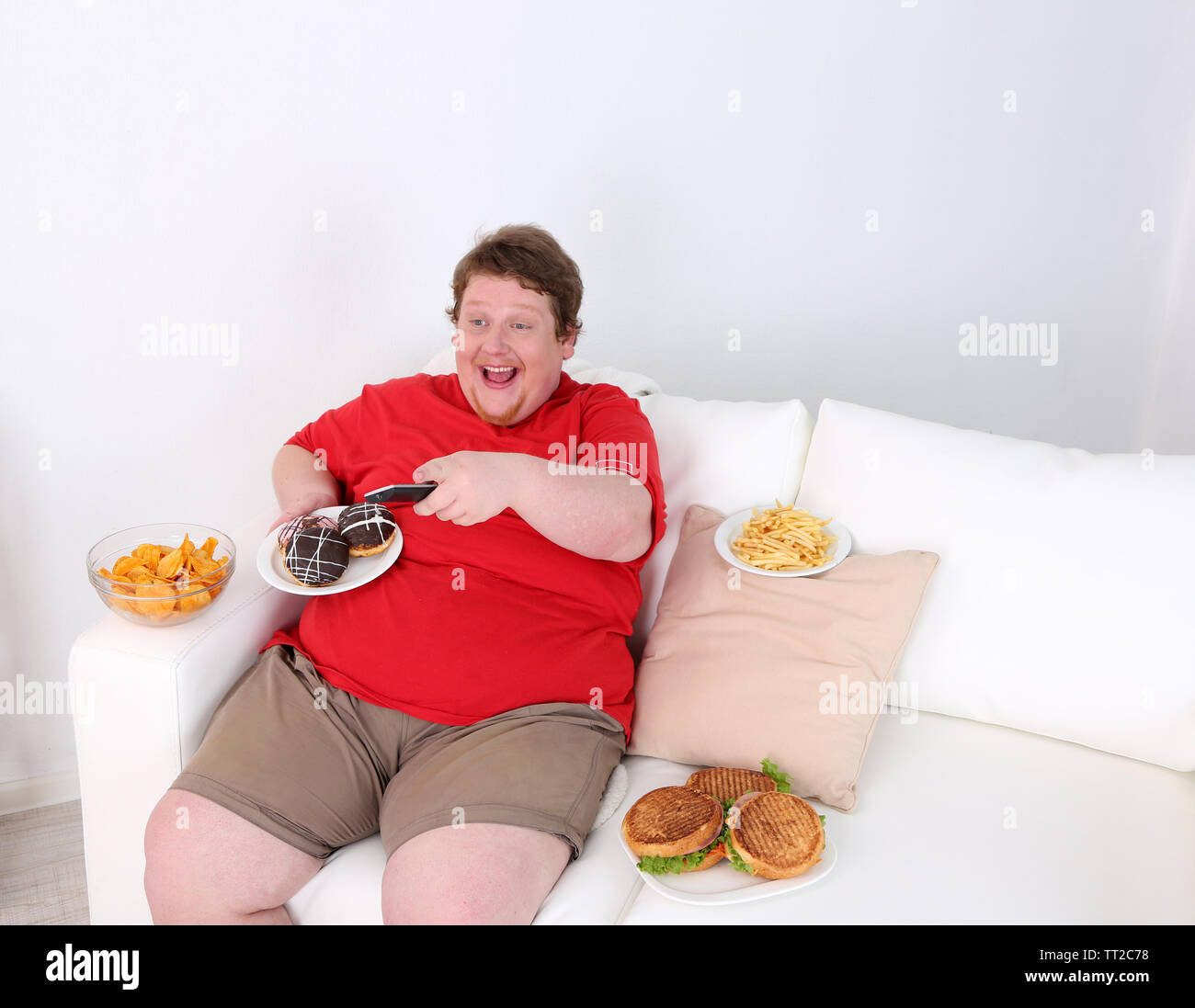 Lazy overweight male sitting with fast food on couch and watching