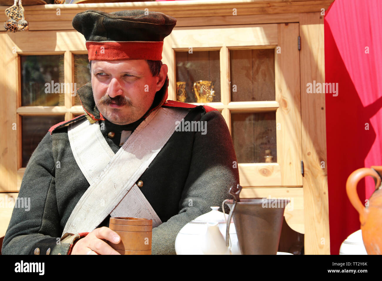 Soldier of the Russian Empire of 19th century sitting with wooden cup in a tavern during the Moscow historical festival Times and Epochs Stock Photo