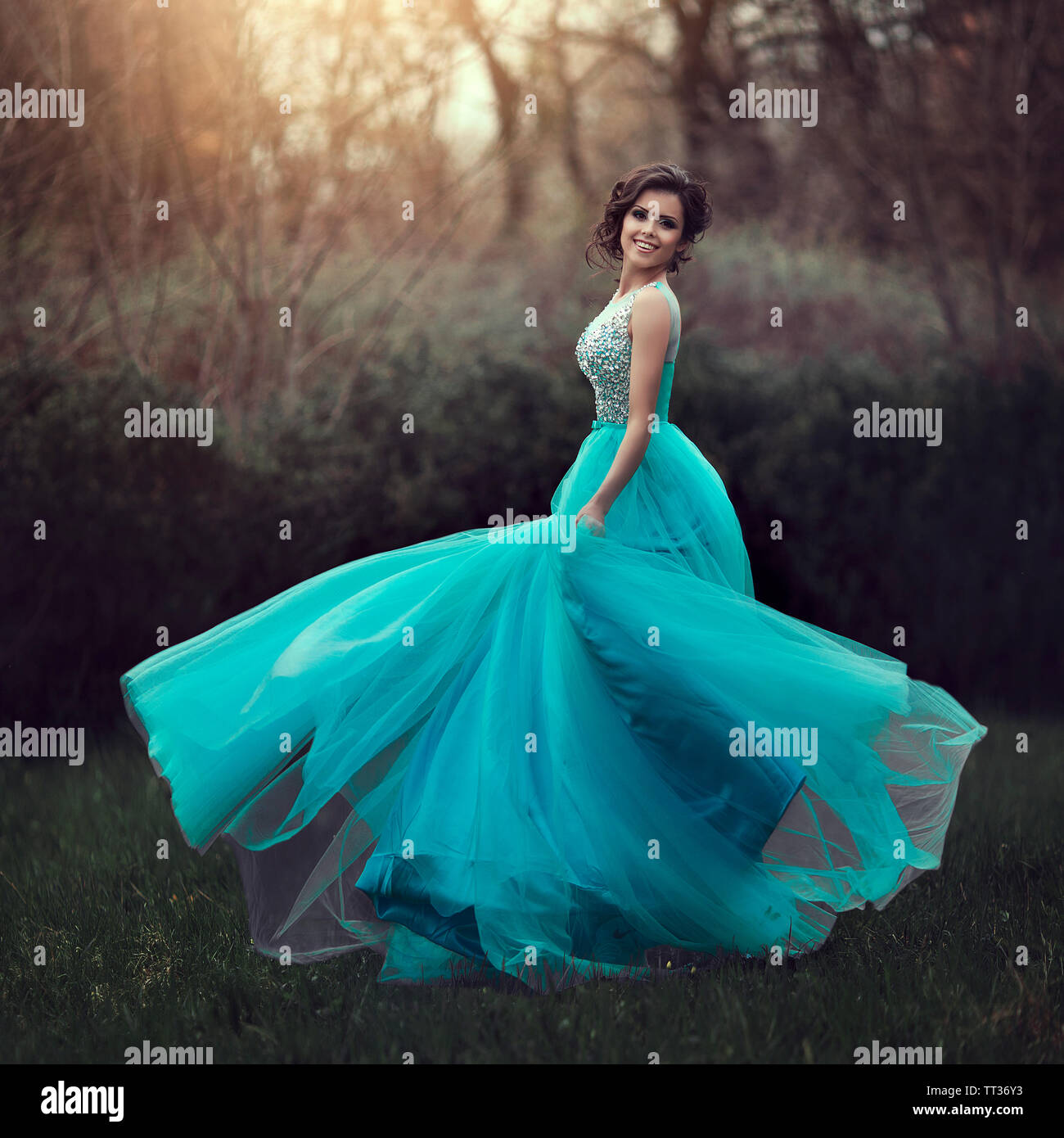 A beautiful graduate girl is spinning in a clearing in a blue dress. Elegant young woman in a beautiful dress in the park. Art photo. Stock Photo