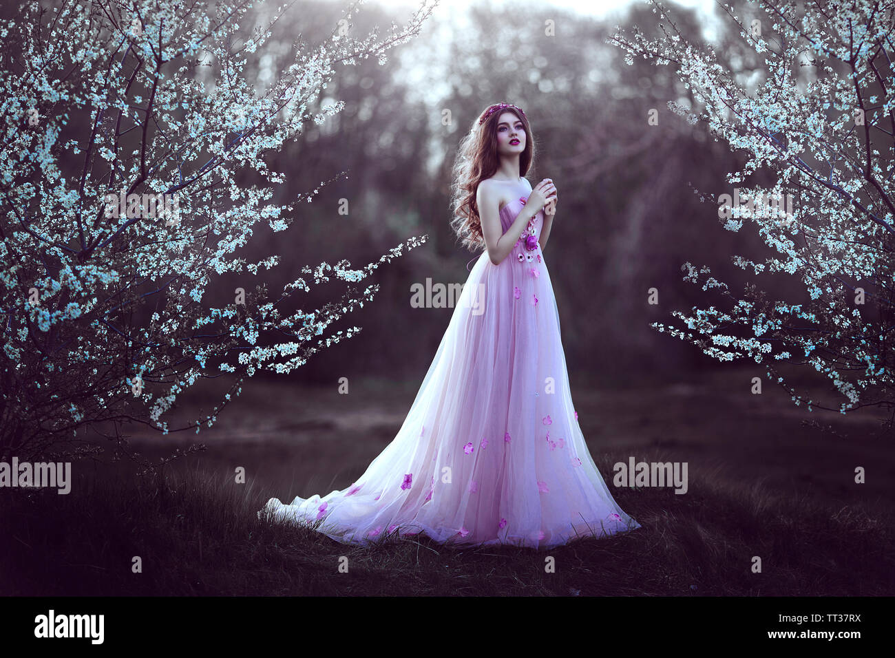 Beautiful Romantic Girl with long hair in fairy long pink dress standing near flowering tree.Fantasy art. Creative colors and Artistic processing. Stock Photo
