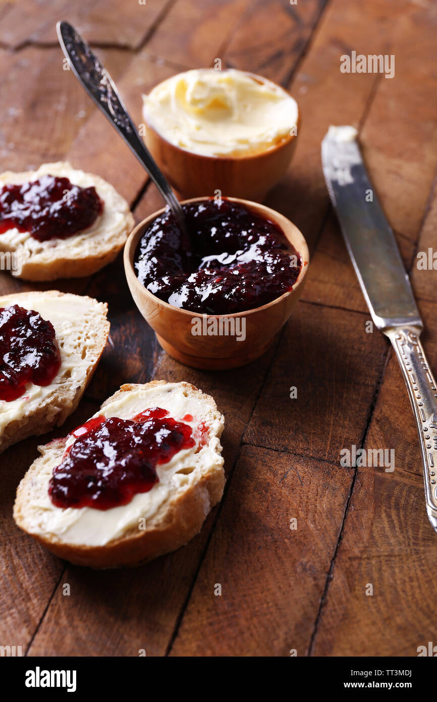 Fresh bread with homemade butter and blackcurrant jam on wooden background Stock Photo