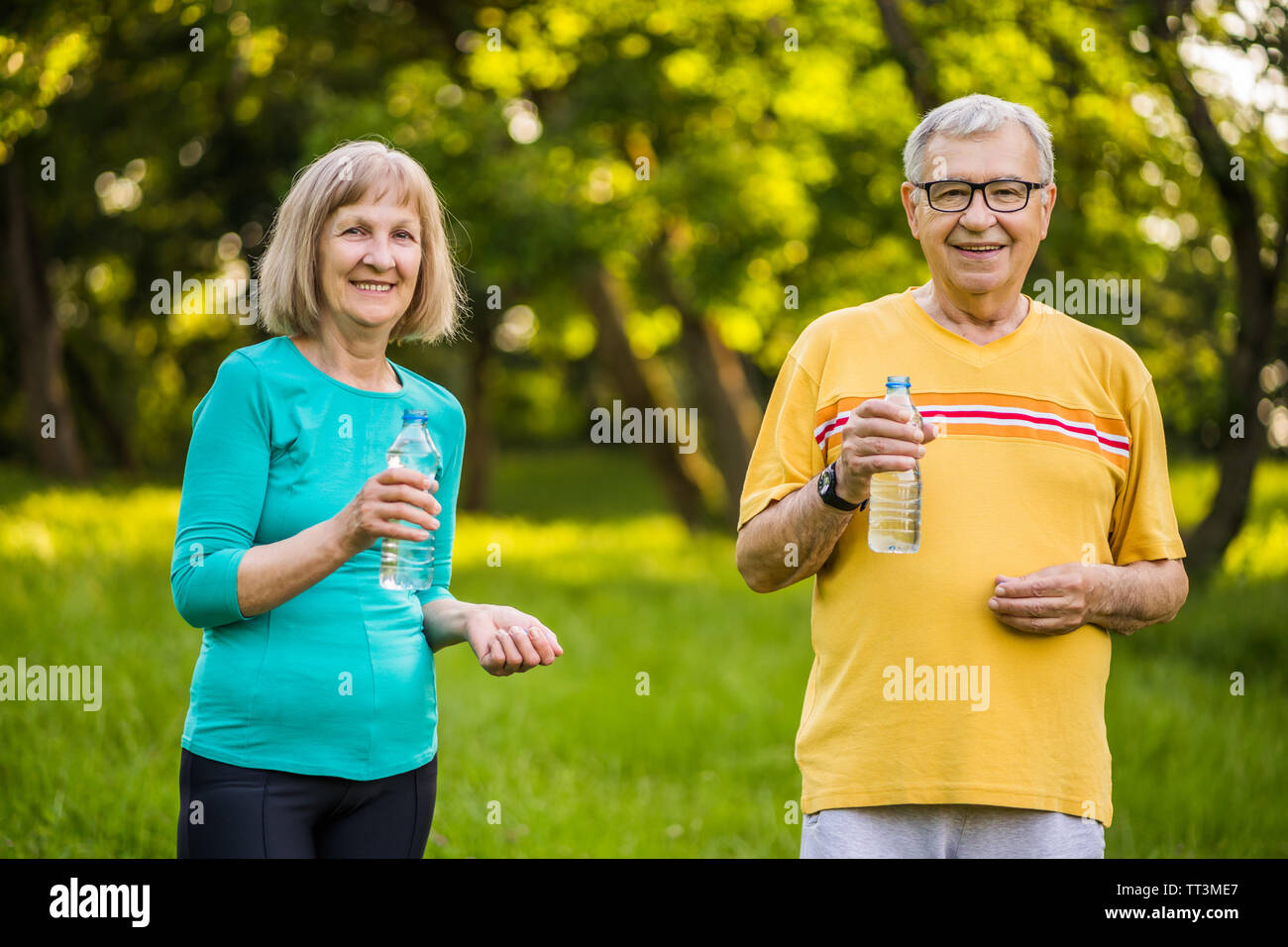 Happy senior couple is drinking water after exercising in park. Stock Photo