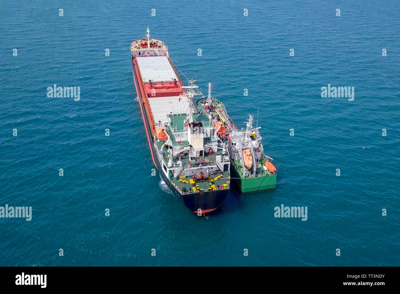 Refuelling at sea - Small Oil products ship fuelling a large Bulk carrier, aerial image. Stock Photo