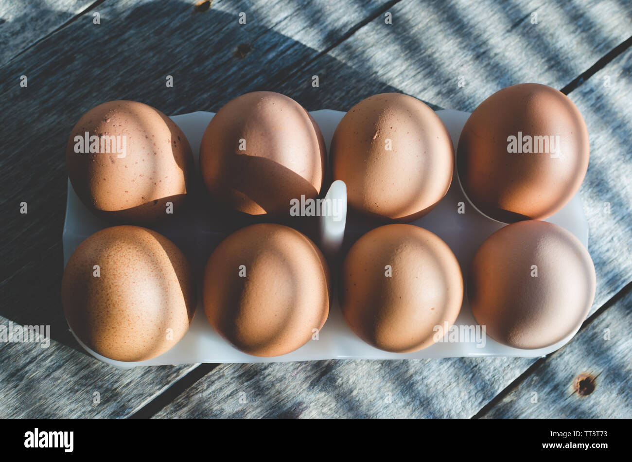 Chicken eggs on a wooden old table in the early sun. The shadows from ...