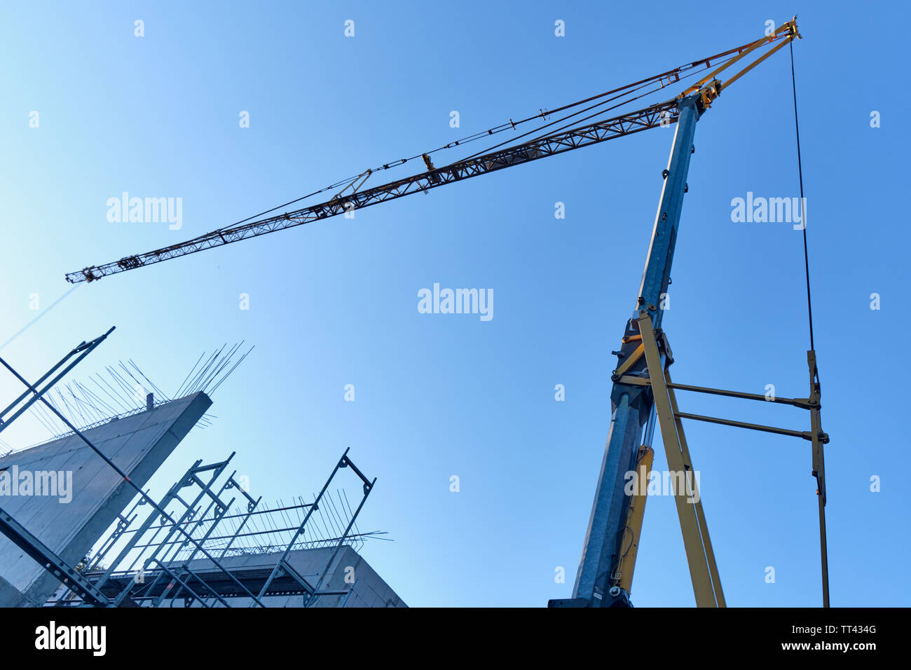 Crane against the blue sky above the shell construction of a house with a scaffolding in the evening light Stock Photo