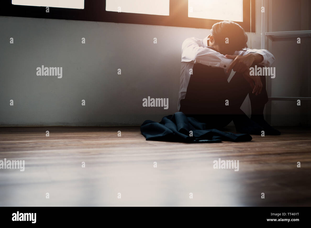 alone depressed man sitting in corner dark room because of problem and sadness in life Stock