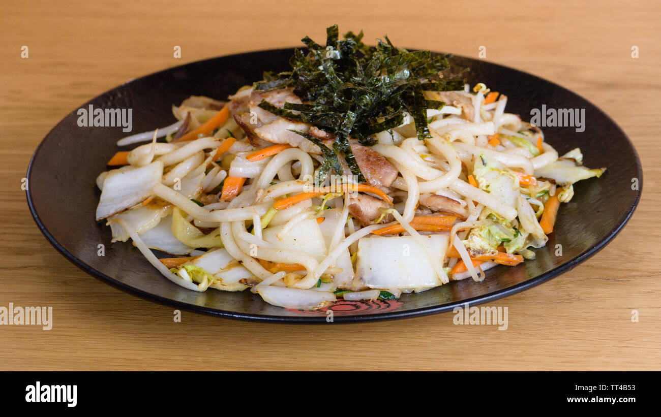 noodles with grilled vegetables and fried seaweed, grilled pork, carrots and soybean sprouts on a circular black plate Stock Photo