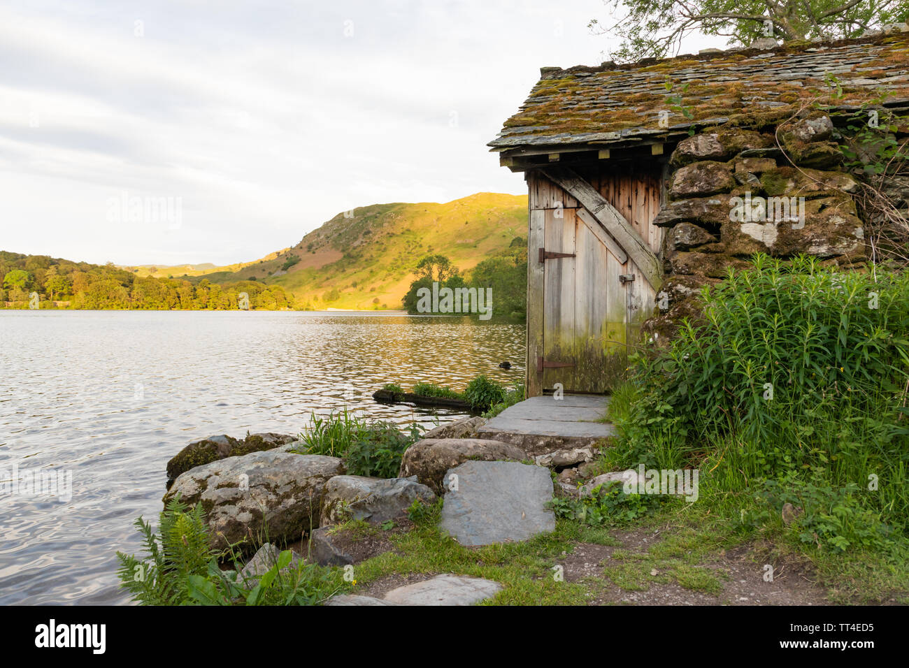 Grasmere, Lake District, Cumbria, UK: A stone boathouse with slate roof and wooden door on the side of Grasmere with Loughrigg Fell in the background. Stock Photo