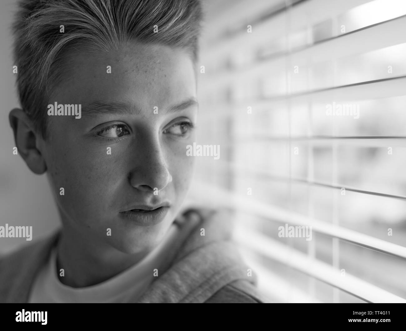 Boy looking out of a window through blinds Stock Photo