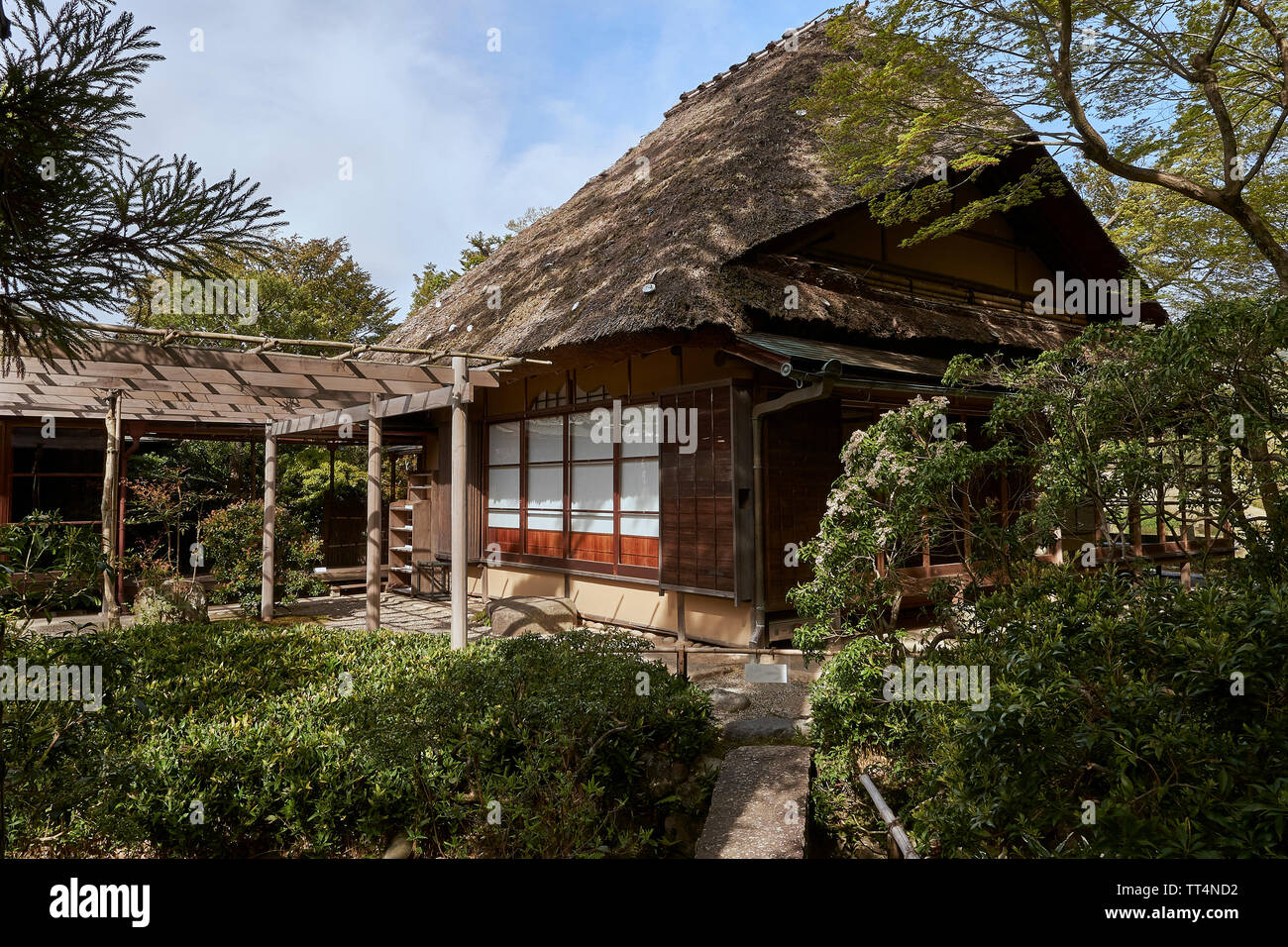 A traditional japanese wooden house, covered with straw. Trees and bushes belong to the park around the house. Stock Photo