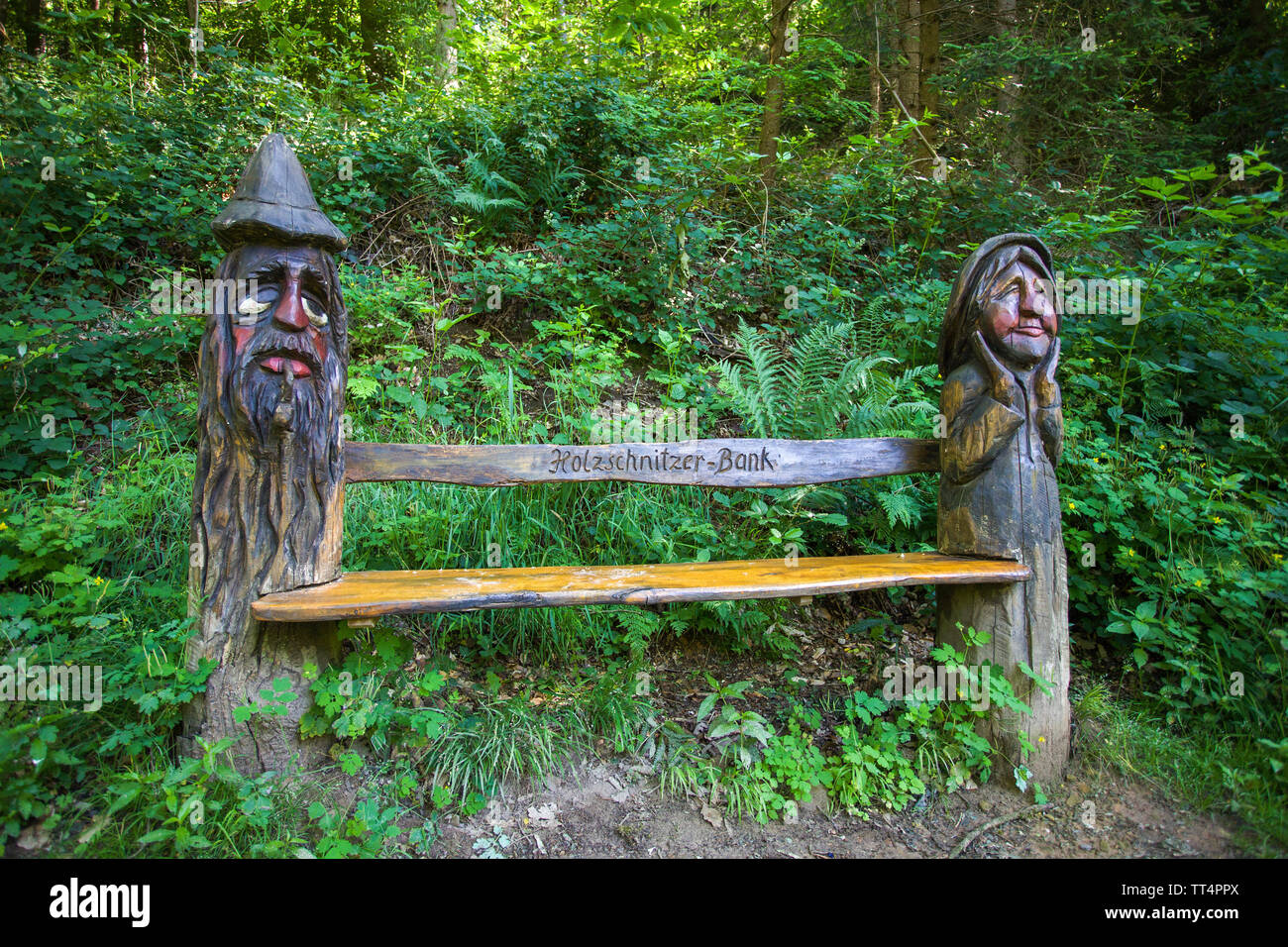 Carved faces on tree trunks, bench seat, forest ghosts trail (german: Waldgeisterweg), Oberotterbach, German Wine Route, Rhineland-Palatinate, Germany Stock Photo
