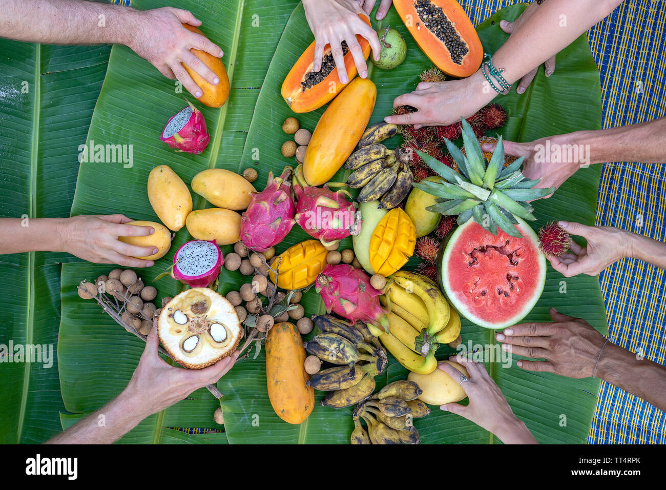 Tropical fruits on green banana leaves and people hands. Group of happy friends having nice food, enjoying the party and communication. Mango, papaya, Stock Photo